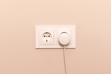 Group of white european electrical outlets with round plug inserted into it on modern beige wall