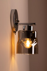 Modern stylish glass sconce lamp on beige wall in bright bedroom