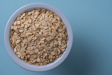 Dry oat flakes in a white plate on a blue background. Heap of oat flakes, top view, close up, copy space