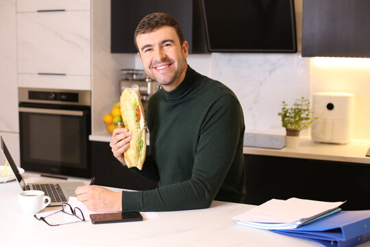 Worker Eating A Very Large Sandwich In Home Office 