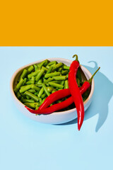 Plate with fresh vegetables, green beans and red chili pepper on blue tablecloth and yellow background. Food pop art photography.