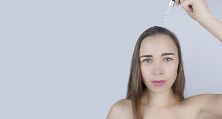 Brunette girl applies oil on her head to strengthen the roots and care for her hair. Means against baldness, brittleness, tarnishing, loss of color, hair strengthening. Concept of care and cosmetology