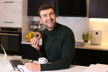 Man eating a doughnut and drinking a coffee in home office 