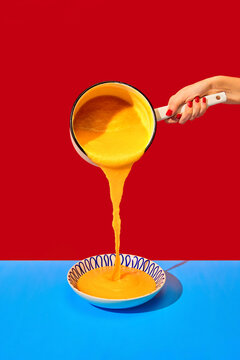 Naklejki Female hand pouring delicious cheese soup into plate on blue tablecloth over red background. French dinner. Food pop art photography.
