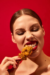 Young woman with red lipstick eating fried chicken, nuggets over vivid red background. Fast food lover. Food pop art photography.