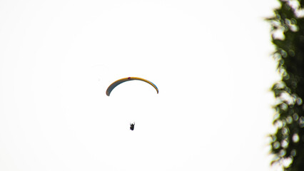 silhoutte of a person paragliding in Miraflores, Lima, Peru 2022 on a cloudy day.  Risk sport.  yellow and blue paraglider.  Peru tourism.