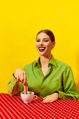 Smiling young woman vintage clothes dipping sausage into coffee cup, cappuccino on red tablecloth...