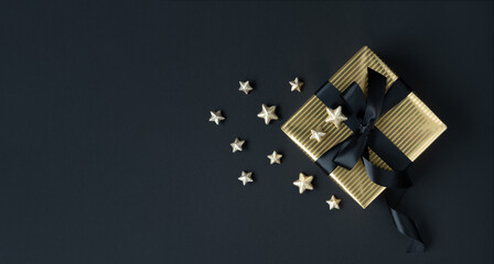 Golden gift box with black ribbon and golden stars on dark background. Space for your text.