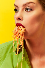 Close-up image of young girl eating spaghetti, noodles sticking out of the mouth over yellow...
