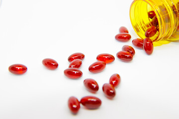 Red round pills poured out of a yellow prescription bottle in white background