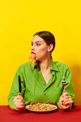 Young girl eating spaghetti, noodles sticking out of the mouth over yellow background. Dinner time. Italian food lover. Food pop art photography.