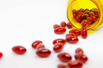 Red round pills poured out of a yellow prescription bottle in white background