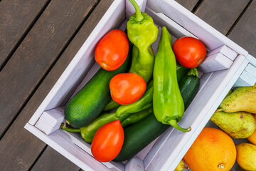 Some fresh fruits and tomatoes with Italian green peppers inside a wooden box seen from the top