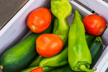 Some fresh fruits and tomatoes with Italian green peppers inside a wooden box
