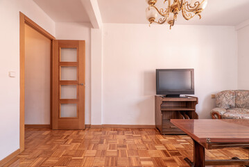 Living room with a TV cabinet, a wooden folding table and a door with transparent square windows with a parquet floor