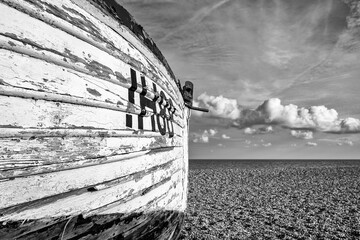Dramatic view of an abandoned wooden fishing boat showing its rough texture. Seen on an empty shingle beach looking at the the North Sea.