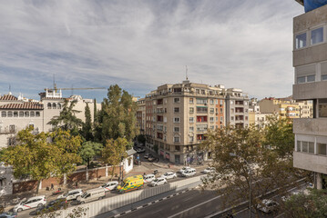 Facades of houses and an avenue with many trees and some traffic