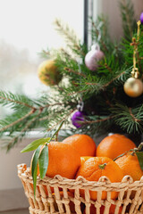 Basket with fresh organic clementines on a windowsill with christmas decoration. Tangerines or mandarin oranges with green leaves. Healthy eating concept.
