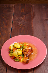 Baked chicken drumstick with vegetables potatoes green beans in sauce and spices on a wooden table.copy space