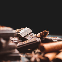Dark chocolate bar pieces on dark background with copy-space, grated chocolate and spices, pile chunks of broken chocolate