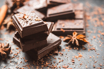 Dark chocolate bar pieces on dark background with grated chocolate and spices, pile chunks of...