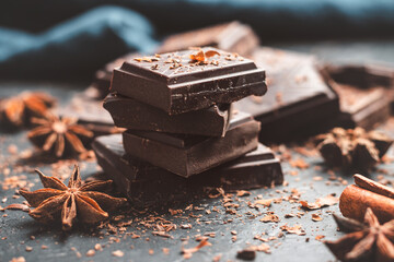 Dark chocolate bar pieces on dark background with grated chocolate and spices, pile chunks of broken chocolate