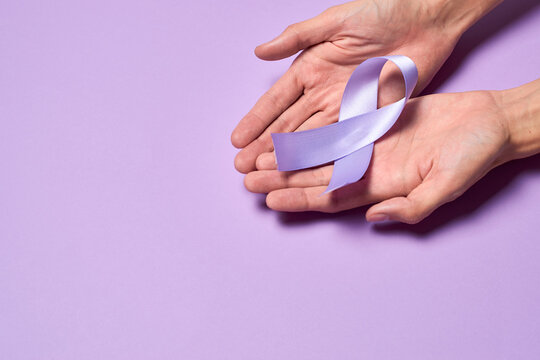 Hands holding purple ribbon, world cancer day february 4th, on purple flat lay.