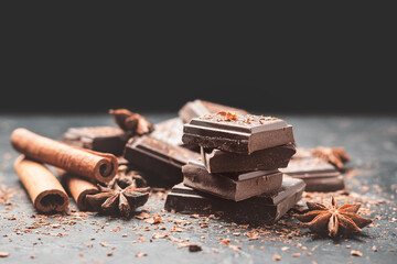 Dark chocolate bar pieces on dark background with copy-space, grated chocolate and spices, pile chunks of broken chocolate