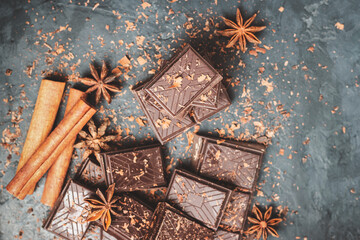 Dark chocolate bar pieces on dark background with grated chocolate and spices, pile chunks of broken chocolate, top view