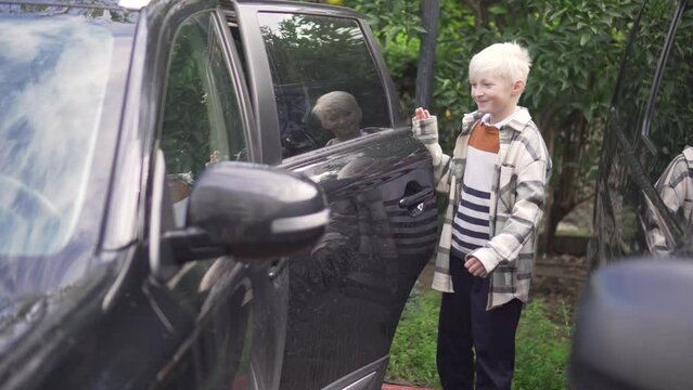 A blond schoolboy gets into the car in the back seat.