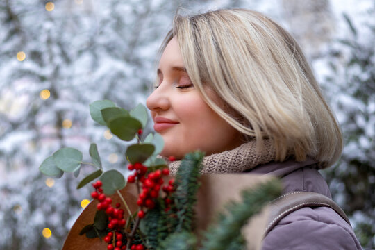 A lonely young woman enjoys a Christmas bouquet in a snowy winter park. Self-love, loneliness in the buzz