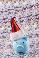 Piggy bank in a Christmas red cap against the background of 100 American dollar bills