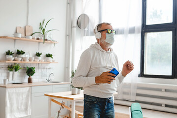 Senior man with medical mask on face dance and using smartphone app for creating playlist music on mobile app - Elderly male having fun dancing with mobile phone technology - Tech and joyful elderly