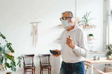 Senior man with medical mask on face dance and using smartphone app for creating playlist music on mobile app copy space - Elderly male having fun dancing with mobile phone technology - Tech and