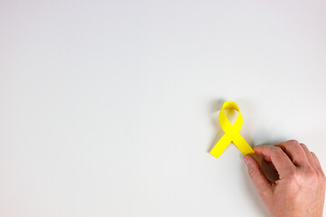Hand holding yellow ribbon on white background, childhood cancer awareness, World cancer day concept, copy space for text