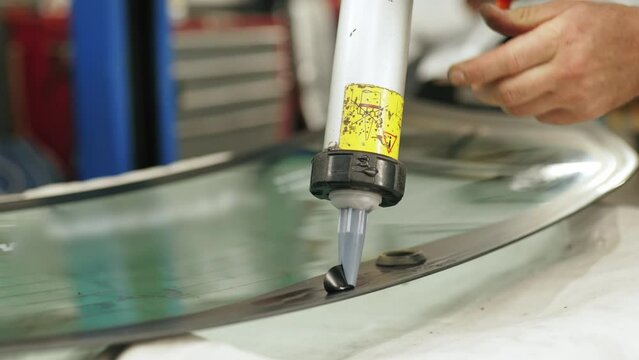 Indoor closeup portrait of white glue gun with black polyurethane glue held by hands of caucasian mechanic and put onto the surface of car window. High quality 4k footage