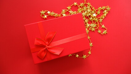 Christmas rectangular, red gift box with ribbon and bow and gold stars on red background. Holiday greeting card