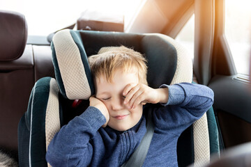 Cute caucasian toddler boy awaken and rub eyes in child safety seat in car during road trip....