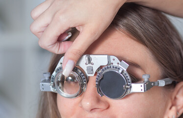 Fototapeta premium a young optometrist girl holds a trial eyeglass frame in her hands, and tries it on to a female patient, the concept of glasses selection, vision correction.