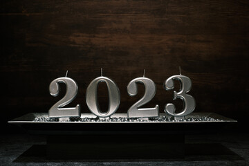 2023 Neues Jahr Silberne Kerzen Schale mit Silberkugeln, im Hintergrund dunkler Holzhintergrund