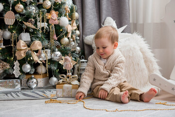 A beautiful little boy is playing with toys on the background of a Christmas tree. The kid is...