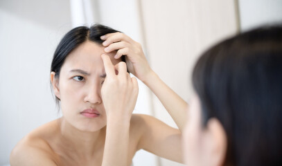 Problem skin. Concerned young asian women popping pimple on cheek while standing near mirror in bathroom. young asian women with acne