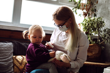 Portrait of little girl toddler sitting on childrens doctor wearing medical mask refusing to get...