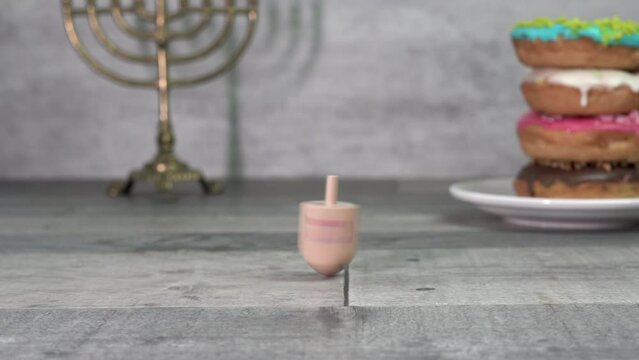 Hand twists a dreidel with the letters Shin, Hey, Nun and Gimel (Hebrew). In the background are hanukkah and donuts. Hanukkah. Jewish holidays (152)