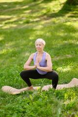 Middle-aged woman doing yoga in the park in the Namaskarasana pose - Sitting Prayer Pose