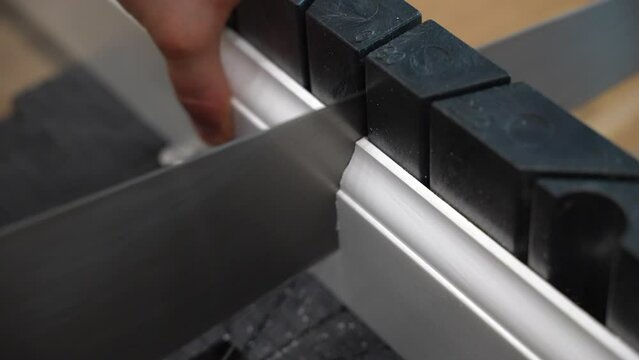 Worker cutting measured white plastic plinth with sharp hand saw at an angle, male preparing baseboard for installing. White sawdust after cutting plastic skirting board with saw, repairing works