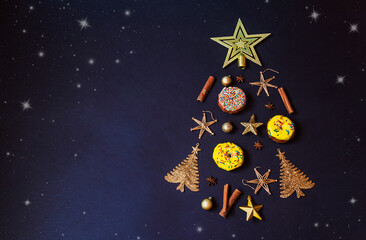 Christmas tree made from golden winter decorations, donuts and spices, on dark background. Holiday...