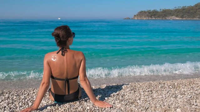 Smiling emoticon lotion. A woman relax on the pebbles beach with smiling spf emoticon lotion on her skin. A concept of healthcare during summer relaxation on the sunny beach.