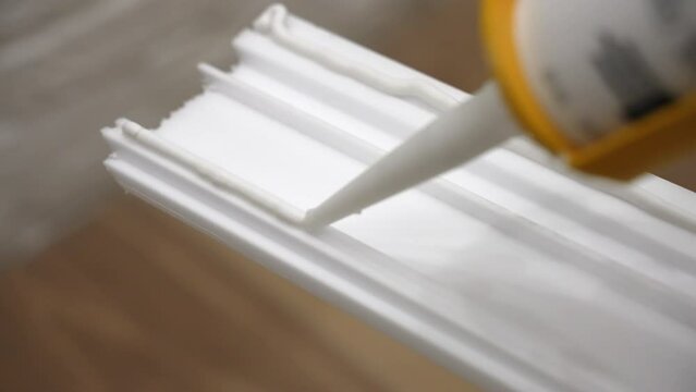 Process of applying white glue on white baseboard surface to fix to the wall, sticky adhesive glue for apartment plinth installation, using glue tube for fixing objects at home