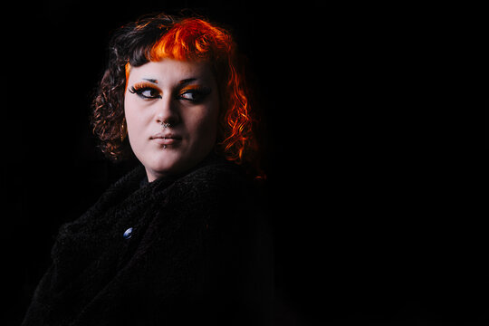 Transgender girl with orange painted hair on a black background.